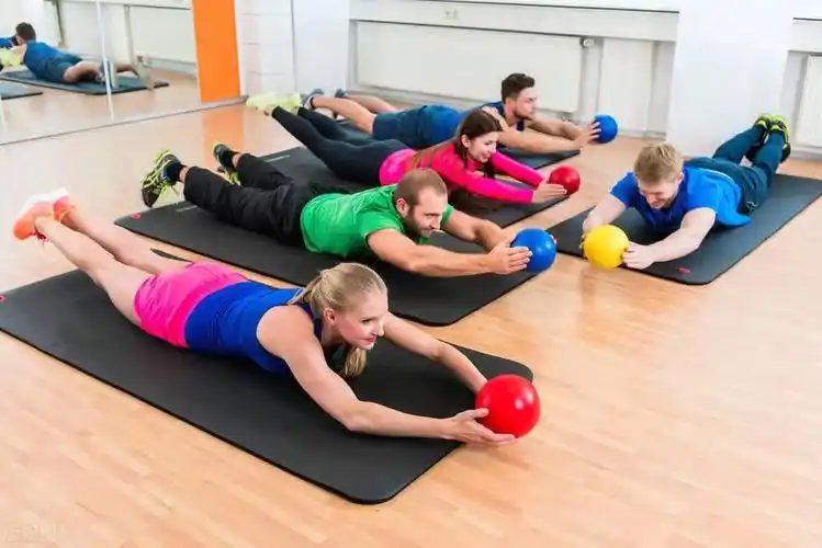 Group workout with small balls in a bright studio, one of many competitors sharing the same audience